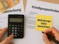 Kündigungsschreiben mit Notiz "Abfindungshöhe berechnen", Taschenrechner und Euro-Scheinen. Berechnung der Abfindung für einen Kleinbetrieb.