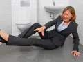 Frau im Anzug stürzt in der Toilette, ein typischer Arbeitsunfall. Sie hält sich den Arm und hat Schmerzen.