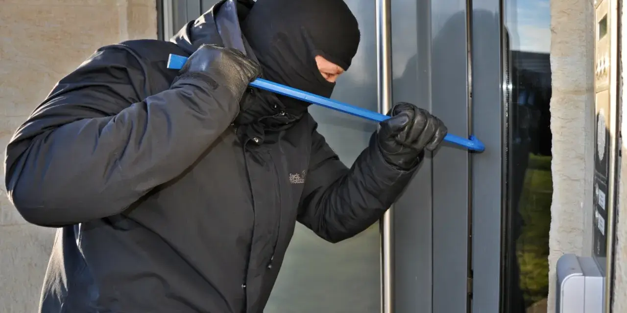 Einbrecher versucht, eine Tür mit einem Brecheisen aufzuhebeln. Wichtig für die Hausratversicherung: Nachweis von Bargeld und Wertgegenständen.