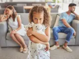 Ein Kind umklammert sein Stofftier, während die Eltern im Hintergrund getrennt sitzen. Ein Bild, das die emotionale Belastung eines Trennungsjahres mit Kindern widerspiegelt.
