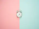 Wecker auf rosa und blauem Hintergrund. Zeit für Stundenreduzierung Schwangerschaft Gehalt.