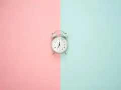 Wecker auf rosa und blauem Hintergrund. Zeit für Stundenreduzierung Schwangerschaft Gehalt.