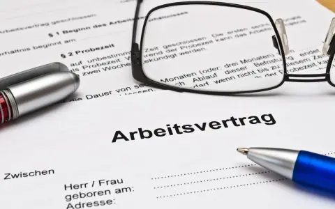 Ein Arbeitsvertrag mit Brille und Stiften liegt bereit. Die Probezeit ist ein wichtiger Teil des Arbeitsvertrags.