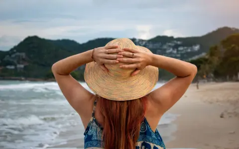 Frauenhände halten Hut am Strand. Endlich Zeit für Urlaub, der gesetzliche Urlaubsanspruch ab 50 ist wohlverdient.