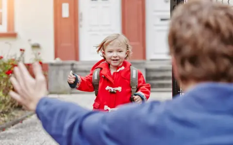 Kleines Mädchen im roten Mantel mit Rucksack rennt auf jemanden zu. Ein schönes Beispiel für das Wechselmodell bei Kindern.