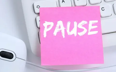 Ein rosa Zettel mit dem Wort "PAUSE" liegt auf einer Tastatur neben einer Maus. Ein Hinweis auf das **bildschirmpause gesetz**.