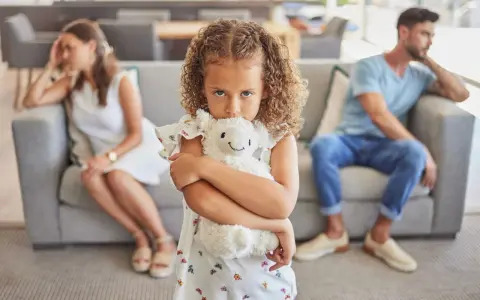 Ein Kind umklammert sein Stofftier, während die Eltern im Hintergrund getrennt sitzen. Ein Bild, das die emotionale Belastung eines Trennungsjahres mit Kindern widerspiegelt.