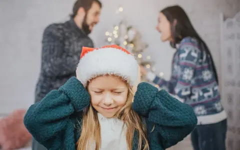 Ein Kind mit Weihnachtsmütze hält sich die Ohren zu, während die Eltern im Hintergrund streiten. Weihnachten trennen sie.