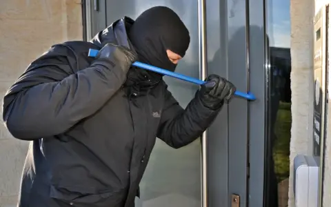 Einbrecher versucht, eine Tür mit einem Brecheisen aufzuhebeln. Wichtig für die Hausratversicherung: Nachweis von Bargeld und Wertgegenständen.