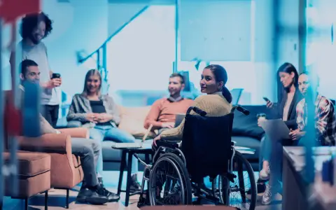 Ein Team bespricht sich, eine Frau im Rollstuhl ist integriert. Ein leidensgerechter Arbeitsplatz, an dem alle willkommen sind.