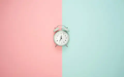 Wecker auf rosa und blauem Hintergrund. Zeit für Stundenreduzierung Schwangerschaft Gehalt.