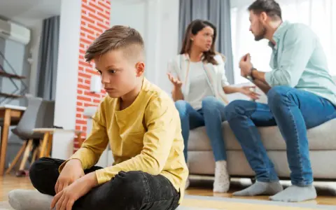 Trauriger Junge sitzt allein, während Eltern streiten. Die Vorteile eines Nebenwohnsitzes für Kinder sind oft, dass sie in einer ruhigeren Umgebung aufwachsen können.