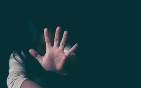 Frau hält Hand vor Gesicht, um sich vor psychischer Gewalt zu schützen. Sie fühlt sich bedroht, vielleicht wegen einer Wohnungszuweisung.