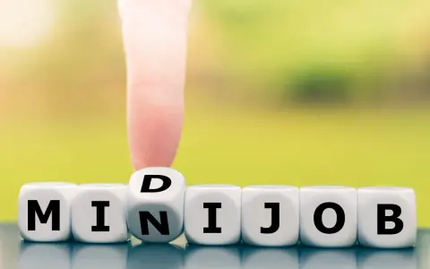 Würfel zeigen "MINIJOB". Ein Finger dreht den Würfel mit "D" zu "N", um "MINIJOB" zu bilden. Ideal für flexible Stunden pro Woche.