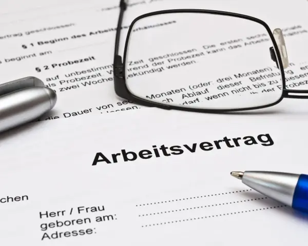 Ein Arbeitsvertrag mit Brille und Stiften liegt bereit. Die Probezeit ist ein wichtiger Teil des Arbeitsvertrags.