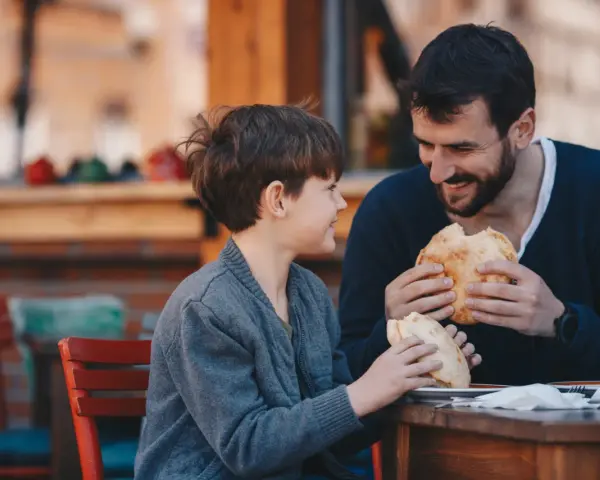 Vater und Sohn teilen sich ein Brot. Vielleicht plant der Vater ein Wechselmodell, um Unterhalt zu sparen, aber im Moment genießen sie die gemeinsame Zeit.