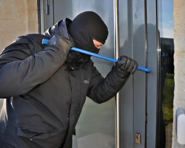Einbrecher versucht, eine Tür mit einem Brecheisen aufzuhebeln. Wichtig für die Hausratversicherung: Nachweis von Bargeld und Wertgegenständen.