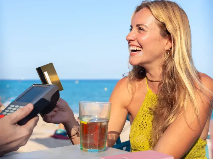 Lachende Frau bezahlt am Strand mit Karte. Selbst mit Krankengeld ist Urlaubsgeld drin!