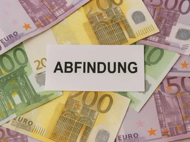 Euro-Scheine liegen unter einem Zettel mit dem Wort "Abfindung". Vielleicht eine finanzielle Unterstützung für jemanden, der mit 64 Jahren in den Ruhestand geht.