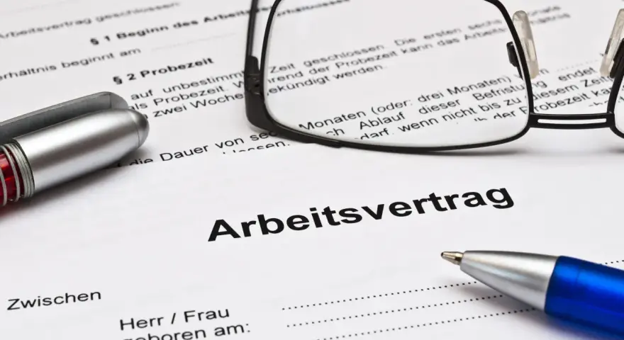 Ein Arbeitsvertrag mit Brille und Stiften liegt bereit. Die Probezeit ist ein wichtiger Teil des Arbeitsvertrags.
