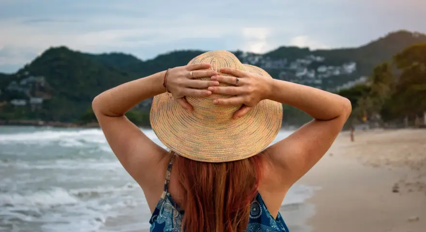 Frauenhände halten Hut am Strand. Endlich Zeit für Urlaub, der gesetzliche Urlaubsanspruch ab 50 ist wohlverdient.