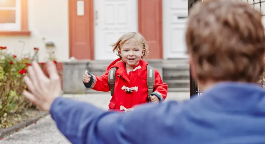 Kleines Mädchen im roten Mantel mit Rucksack rennt auf jemanden zu. Ein schönes Beispiel für das Wechselmodell bei Kindern.