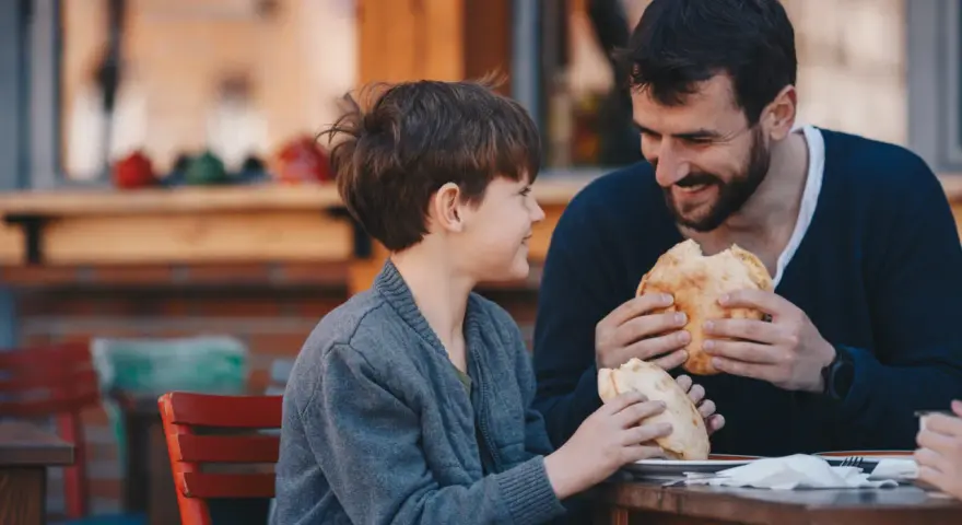 Vater und Sohn teilen sich ein Brot. Vielleicht plant der Vater ein Wechselmodell, um Unterhalt zu sparen, aber im Moment genießen sie die gemeinsame Zeit.