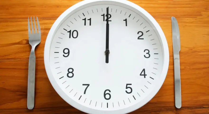 Uhr zeigt 12 Uhr. Gabel und Messer liegen bereit. Zeit für die Mittagspause während der Arbeitszeit.
