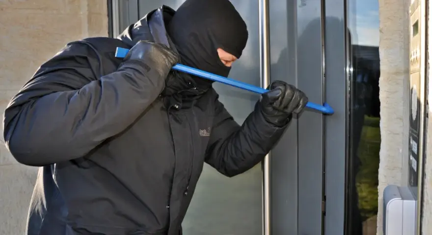 Einbrecher versucht, eine Tür mit einem Brecheisen aufzuhebeln. Wichtig für die Hausratversicherung: Nachweis von Bargeld und Wertgegenständen.