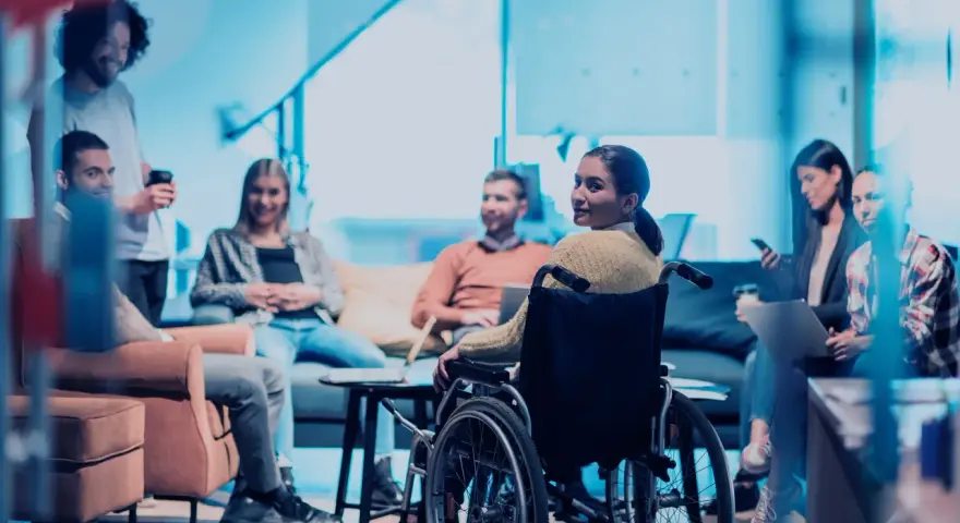 Ein Team bespricht sich, eine Frau im Rollstuhl ist integriert. Ein leidensgerechter Arbeitsplatz, an dem alle willkommen sind.