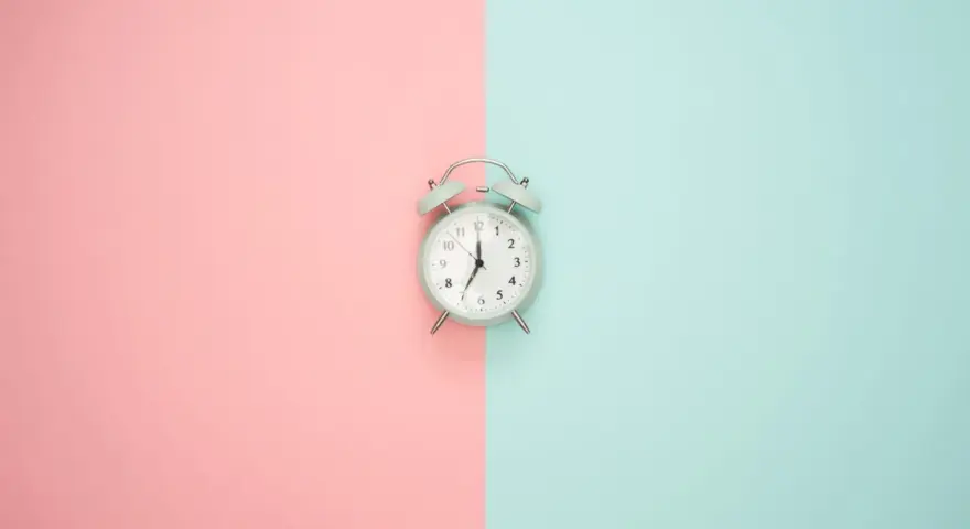 Wecker auf rosa und blauem Hintergrund. Zeit für Stundenreduzierung Schwangerschaft Gehalt.
