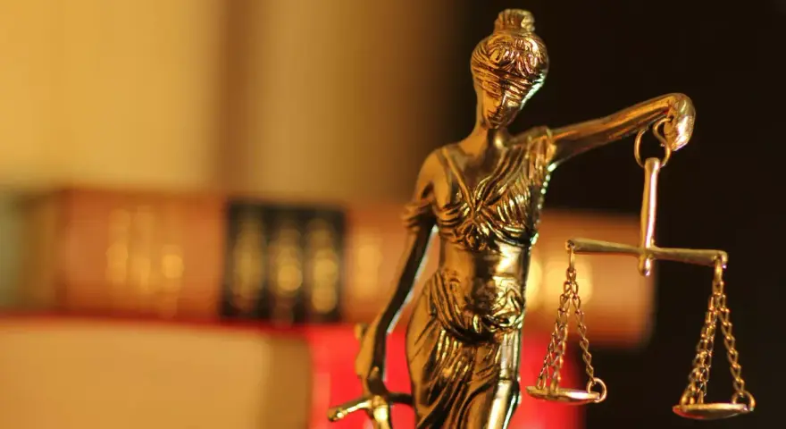 Justitia-Statue mit Waage und Schwert, symbolisiert Gerechtigkeit. Im Hintergrund unscharfe Bücher, die auf einen Fall mit 1/3 Betreuung hindeuten könnten.