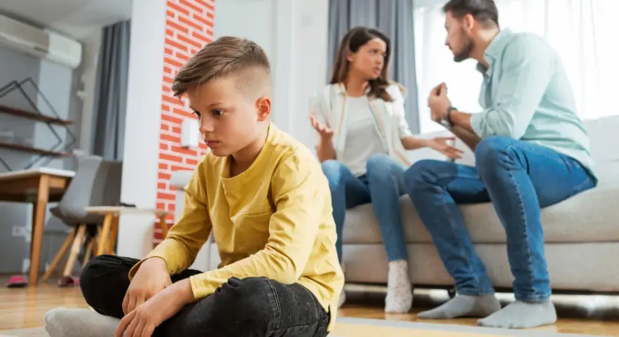 Trauriger Junge sitzt allein, während Eltern streiten. Die Vorteile eines Nebenwohnsitzes für Kinder sind oft, dass sie in einer ruhigeren Umgebung aufwachsen können.