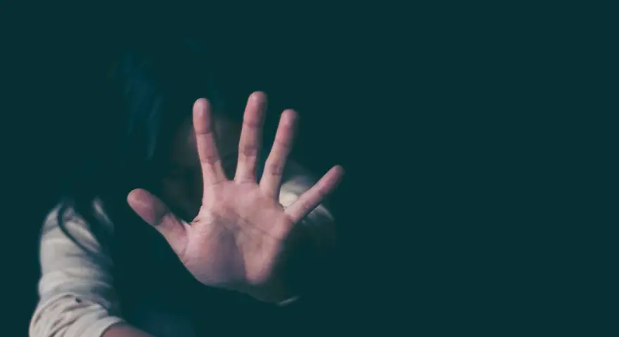 Frau hält Hand vor Gesicht, um sich vor psychischer Gewalt zu schützen. Sie fühlt sich bedroht, vielleicht wegen einer Wohnungszuweisung.
