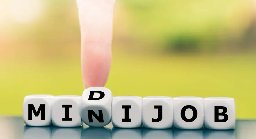 Würfel zeigen "MINIJOB". Ein Finger dreht den Würfel mit "D" zu "N", um "MINIJOB" zu bilden. Ideal für flexible Stunden pro Woche.