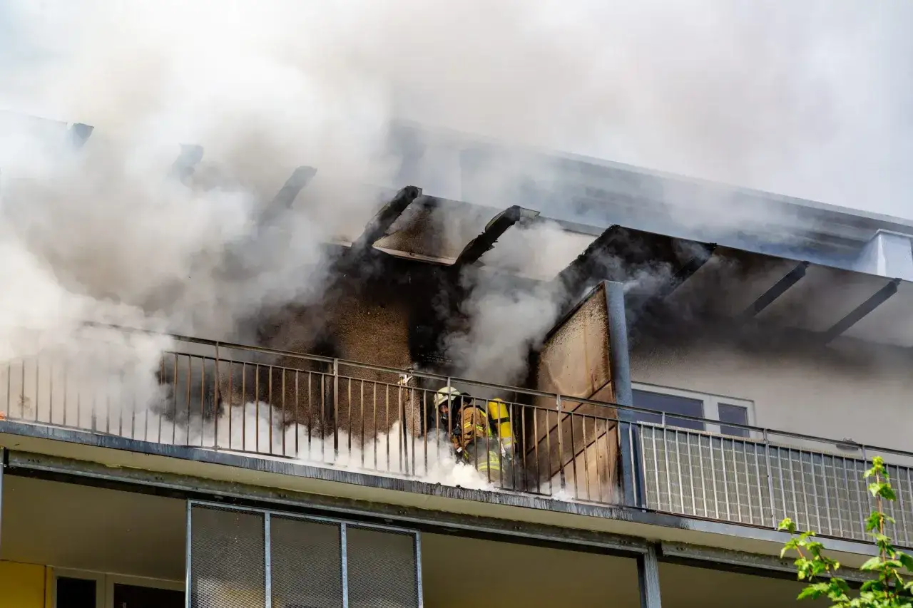 Feuerwehrleute kämpfen gegen einen Brand auf einem Balkon. Ein wichtiger Nachweis für die Hausratversicherung, falls der Brand durch Fahrlässigkeit entstand.