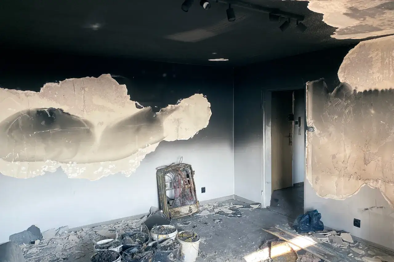 Schwarzer Rauch bedeckt Decke und Wände nach einem wohnungsbrand. Verbrannter Heizkörper und Bauschutt zeugen von der Zerstörung. Eine Versicherung hilft bei der Wiederherstellung.